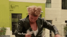 a man wearing a black leather jacket is standing in front of a green building .