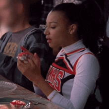 a cheerleader in a vhs uniform holds a cupcake in her hand
