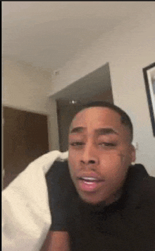 a man in a black shirt is laying on a bed with a white blanket and making a funny face .