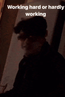 a young man wearing sunglasses and a black jacket is sitting in front of a wall .