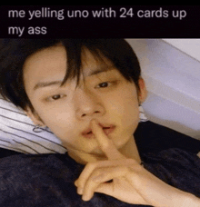 a young man is laying on a bed with his finger to his mouth and the caption says me yelling uno with 24 cards up