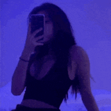 a woman is taking a selfie with her phone in a dark room with blue lights .