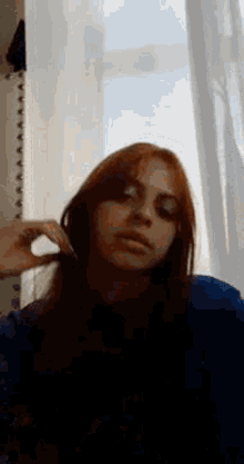 a woman with long red hair is standing in front of a window and brushing her hair .