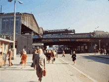 a group of people walking under a bridge that says " bahnhof friedrichstrasse "