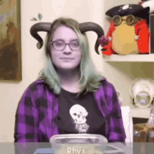 a woman wearing horns and glasses sits at a table with a container that says rhys