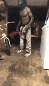 a man without a shirt is standing in a garage next to a bike