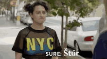 a woman wearing a nyc shirt is standing in front of a white car .