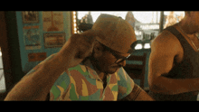 a man wearing a hat and glasses adjusts his hat