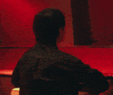 a man with a tattoo on his back is sitting in front of a red wall