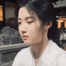 a woman wearing a white kimono and earrings looks down at something