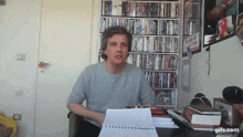 a man is sitting at a desk in front of a bookshelf filled with books .