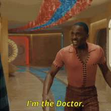 a man in a pink shirt is talking to another man and says " i 'm the doctor "