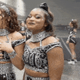 two cheerleaders are standing next to each other and one of them is wearing a black and silver outfit .