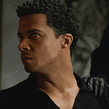 a man with curly hair and a black shirt looks to the side