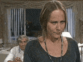 a woman wearing a necklace looks at the camera while a man looks on