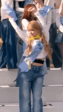 a woman in a white shirt and blue jeans is standing on a stage with her arms in the air .