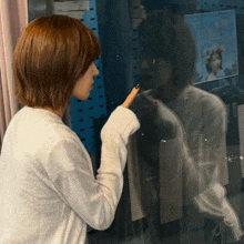 a woman in a white sweater is pointing at a reflection of herself in a mirror