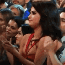 a woman in a red dress is sitting in a crowd of people and clapping .