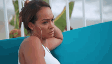 a woman in a white tank top is sitting on a blue couch looking at the camera .