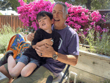 a man in a purple shirt is holding a young boy in his arms