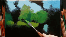 a person is using a palette knife to paint a picture of trees on a black background