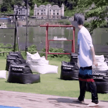a man in a white shirt is walking in front of bean bag chairs that say " camping square "