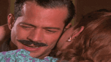 a man with a mustache is hugging a woman who is wearing pearl earrings