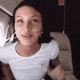 a woman is sitting on a plane wearing a white t-shirt and earrings and smiling .