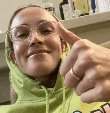a woman wearing glasses and a green hoodie giving a thumbs up sign