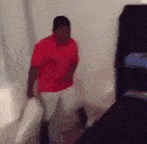 a man in a red shirt and white pants is walking in a room .