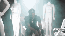 a man in a black shirt is sitting in front of a group of naked mannequins
