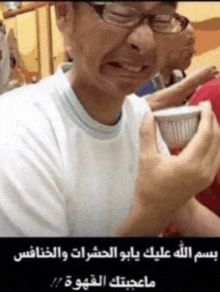 a man wearing glasses and a white shirt is holding a cup with arabic writing on it