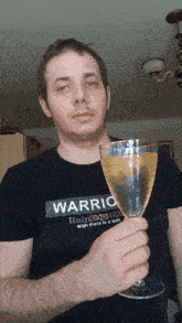 a man wearing a shirt that says warrio holds a glass of wine