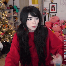 a girl wearing a red sweater is standing in front of a christmas tree