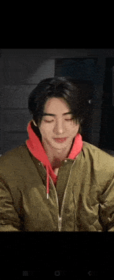 a man wearing a green jacket and a red hoodie is smiling with his eyes closed .