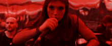a woman singing into a microphone with a man playing drums behind her