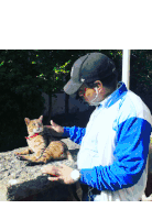 a man in a blue and white jacket petting a cat with a red collar
