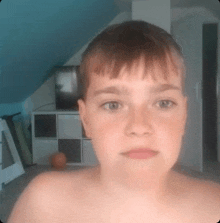 a boy without a shirt is looking at the camera in a room