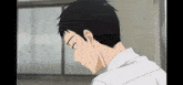 a man with black hair and a white shirt is looking down at something in a room .
