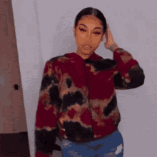 a woman in a tie dye jacket and jeans is standing in front of a white wall .