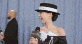 a woman wearing a black and white hat is holding a microphone .