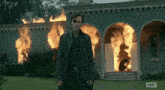 a man with an eye patch is standing in front of a burning building with the letters a and c on the bottom