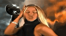 a woman is blowing a kiss while holding a football helmet in front of her head .