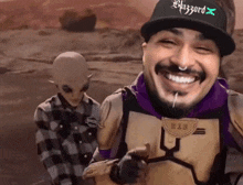 a man wearing a hat that says blizzard on it smiles in front of an alien