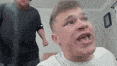 a man in a white shirt is making a funny face while another man looks on .