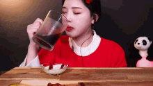 a woman in a red sweater is drinking from a glass while sitting at a table .