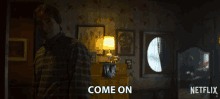a man in a plaid shirt is standing in a dark room and says come on