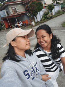 two girls standing next to each other one wearing a hoodie that says " sak "