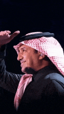 a man wearing a turban and a black shirt holds his hand to his forehead