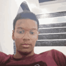 a young man wearing glasses and a maroon shirt looks at the camera